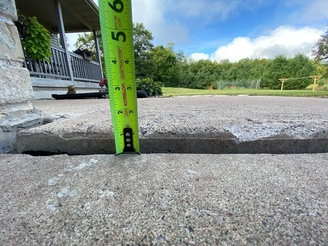 Measuring a sunken concrete slab drop near the home foundation in Shell Lake, WI during inspection.