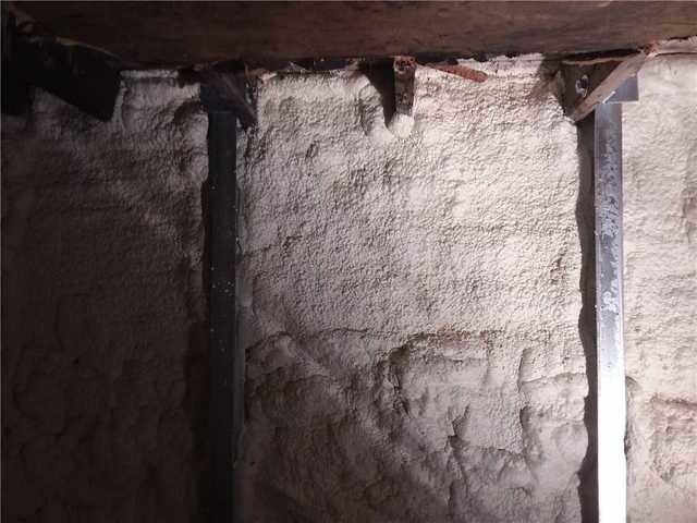 Heavy-duty steel PowerBrace columns installed along a basement foundation wall covered in off-white polyurethane spray foam insulation near Cloquet, MN.