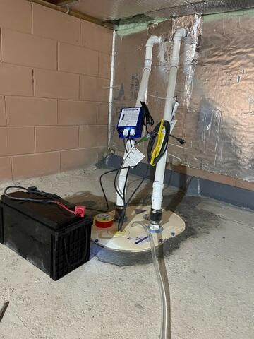 A newly installed heavy-duty TripleSafe sump pump system with clear lids, white PVC discharge lines, and a large black standby battery backup box on a concrete floor in Cornell, WI.