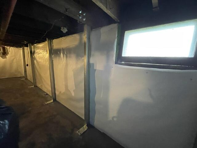 Clean white basement wall liners anchored behind heavy-duty steel foundation stabilization beams in Superior, WI.