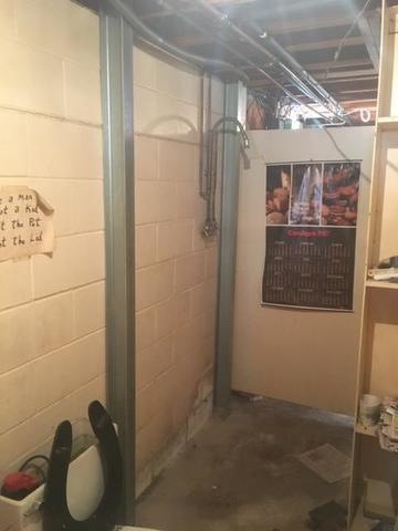 An immaculate basement view showing two high-tensile steel PowerBrace support columns vertically installed against a concrete block foundation wall near basement utility plumbing in Chippewa Falls, WI.