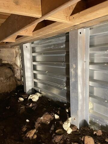 An immaculate view inside a crawl space in Frederic, WI featuring two vertical steel I-beams cleanly bracing an EverBrace corrugated foundation wall support system.