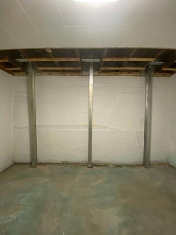 A completed foundation repair project in Ashland, WI showing three vertical steel PowerBrace support columns tightly installed to stabilize a white basement wall.