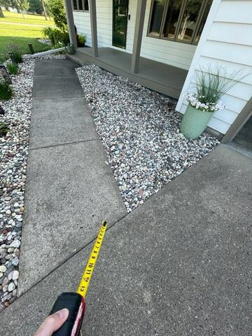 Measuring uneven concrete walkway slabs with a yellow level tool during an inspection in Eau Claire WI