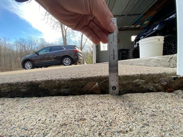 Measuring a significant gap under a sunken concrete slab with a ruler during an inspection in Frederic, WI.