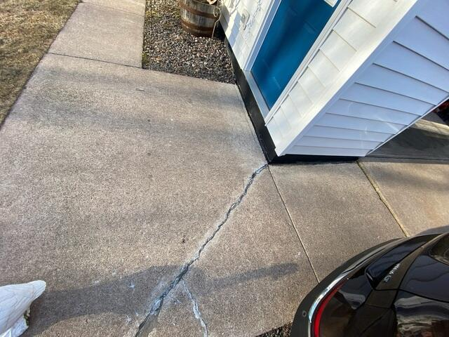 Cracked and uneven concrete sidewalk slabs creating a tripping hazard near a residential home in Frederic, WI.
