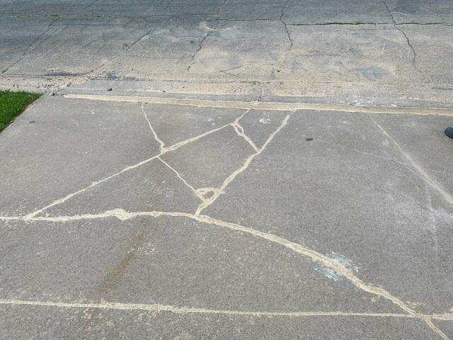 Cracked concrete driveway slab in front of a garage before leveling repair in Menomonie WI