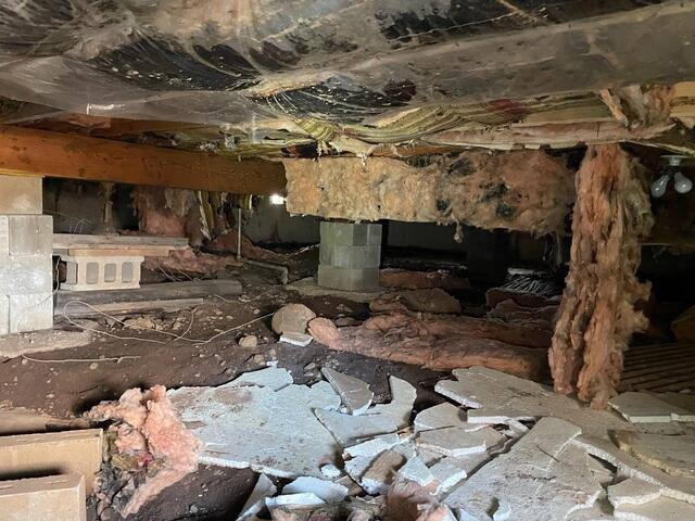A messy, unconditioned crawl space filled with scattered pink fiberglass insulation, dirt, debris, and shifting concrete block stacks in Cloquet, MN before repair.