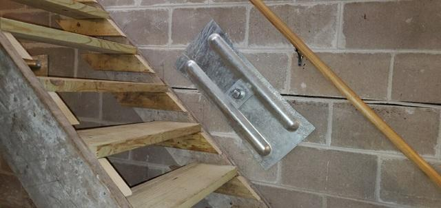 A close-up view of a heavy steel GeoLock wall anchor plate cleanly installed directly over a horizontal mortar crack line in a Comstock, WI basement.