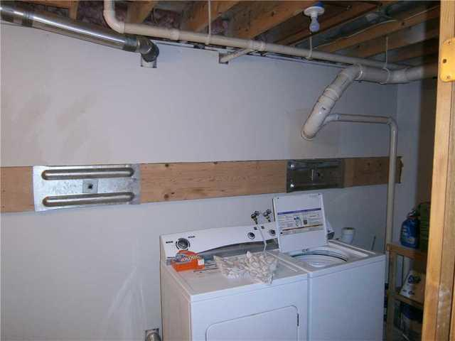 A completed foundation repair project showing a horizontal wooden beam and two heavy steel Geo-Lock wall anchor plates installed behind laundry appliances in Phillips, WI.