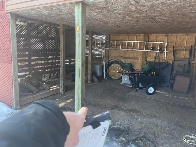A DBS inspector pointing out a settling timber post beneath an elevated home addition and open utility carport storage area in Bethel, MN.