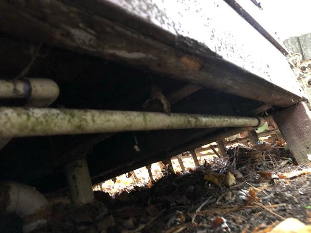 Under framing foundation view of helical pier extensions driven into the ground beneath a cabin structure