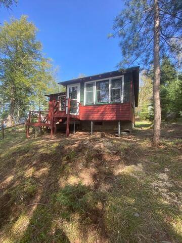 red-residential-cabin-wooded-slope-mercer-wi An exterior view of a red residential cabin built on a grassy, wooded hill with pine trees in Mercer, WI.