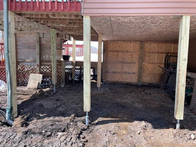 A row of heavy-duty pressure-treated wood posts neatly mounted onto adjustable steel helical pier brackets inside a mud excavation area in Bethel, MN.